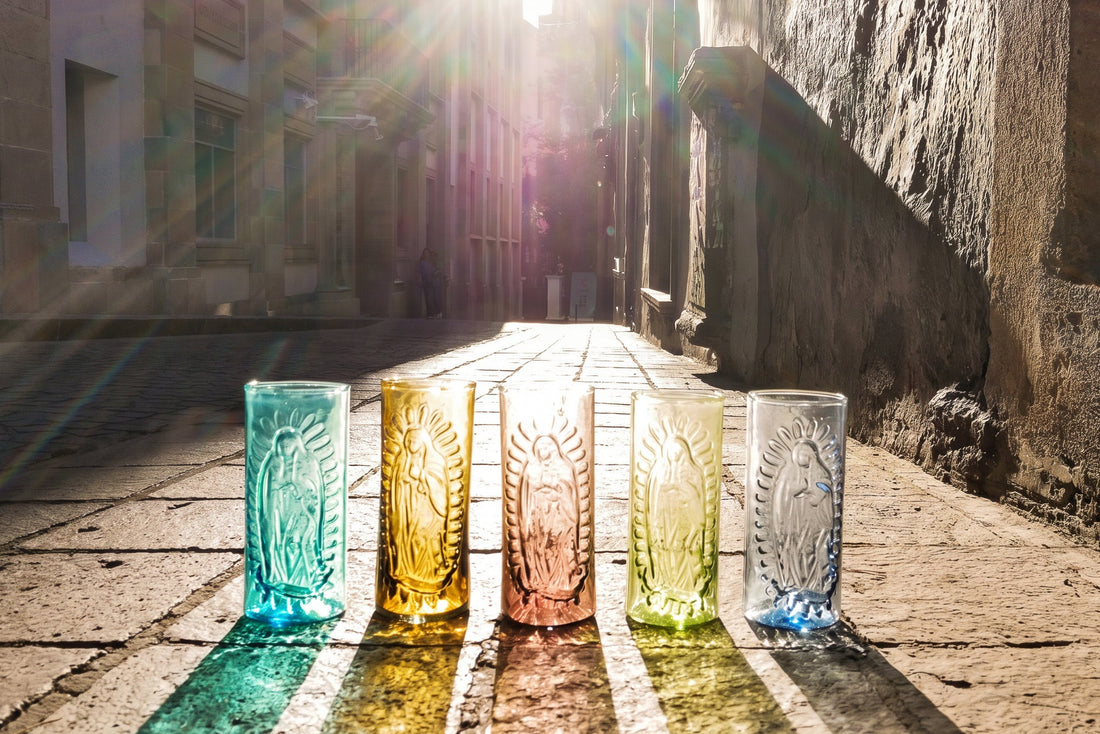 Five colorful glass tumblers with embossed designs on a stone pavement.