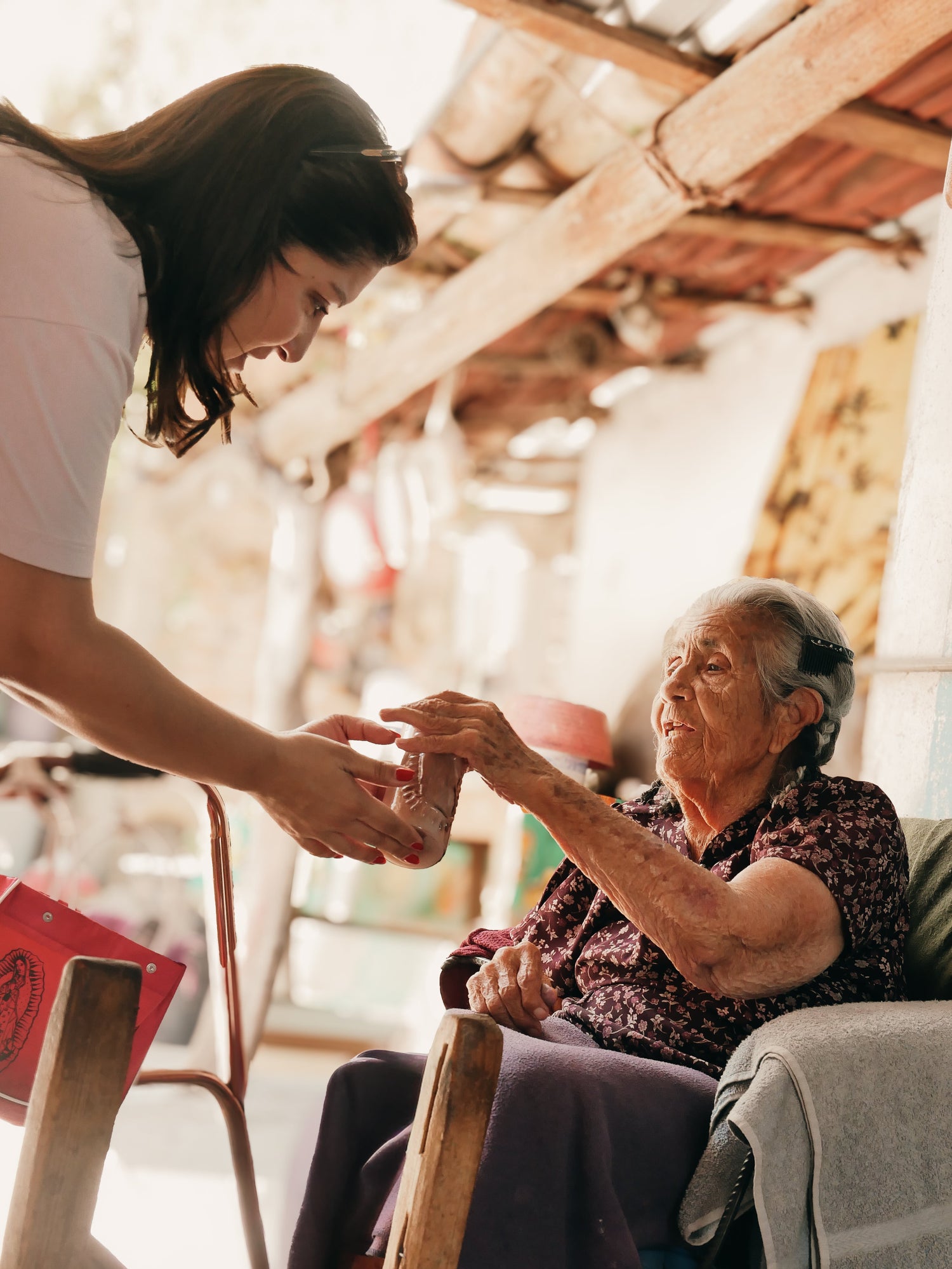 An elderly woman receiving a small object from a younger person in a home setting.